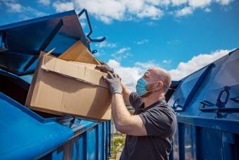 A man wearing a disposable protective mask recycling cardboard boxes at a local environmental recycling centre in the daytime