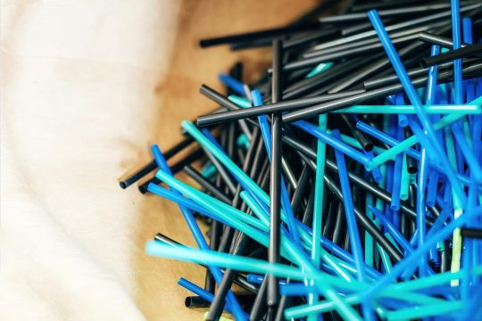 Paper bag containing blue and black plastic straws, recycling materials in a shop.