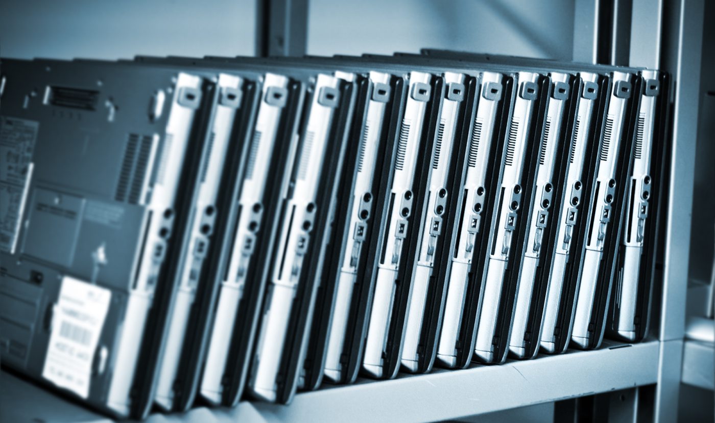 Refurbished silver laptops in a row on a metal shelf