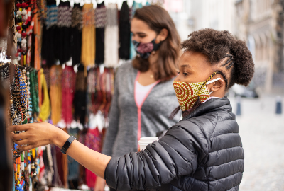 Young woman wearing a protective face mask browsing colourful necklaces outside at a street market stall