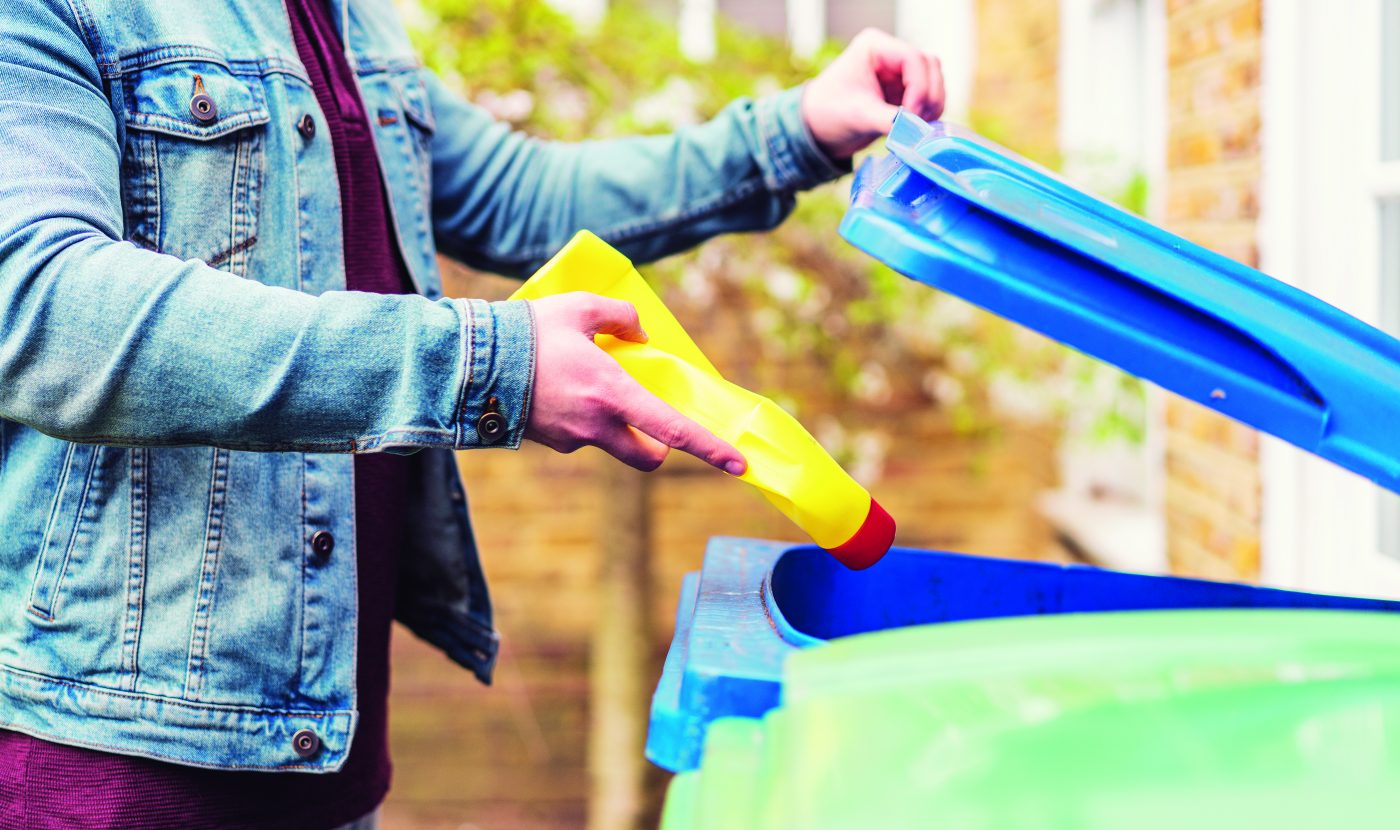 Someone placing a yellow bottle of bleach into a blue recycling bin