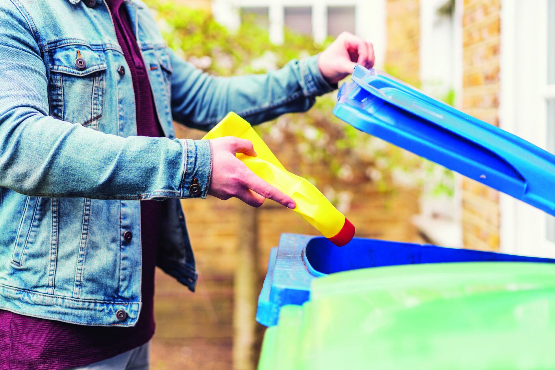 Someone placing a yellow bottle of bleach into a blue recycling bin