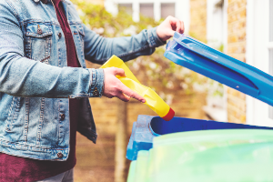 Someone placing a yellow plastic bottle of bleach into a blue recycling bin