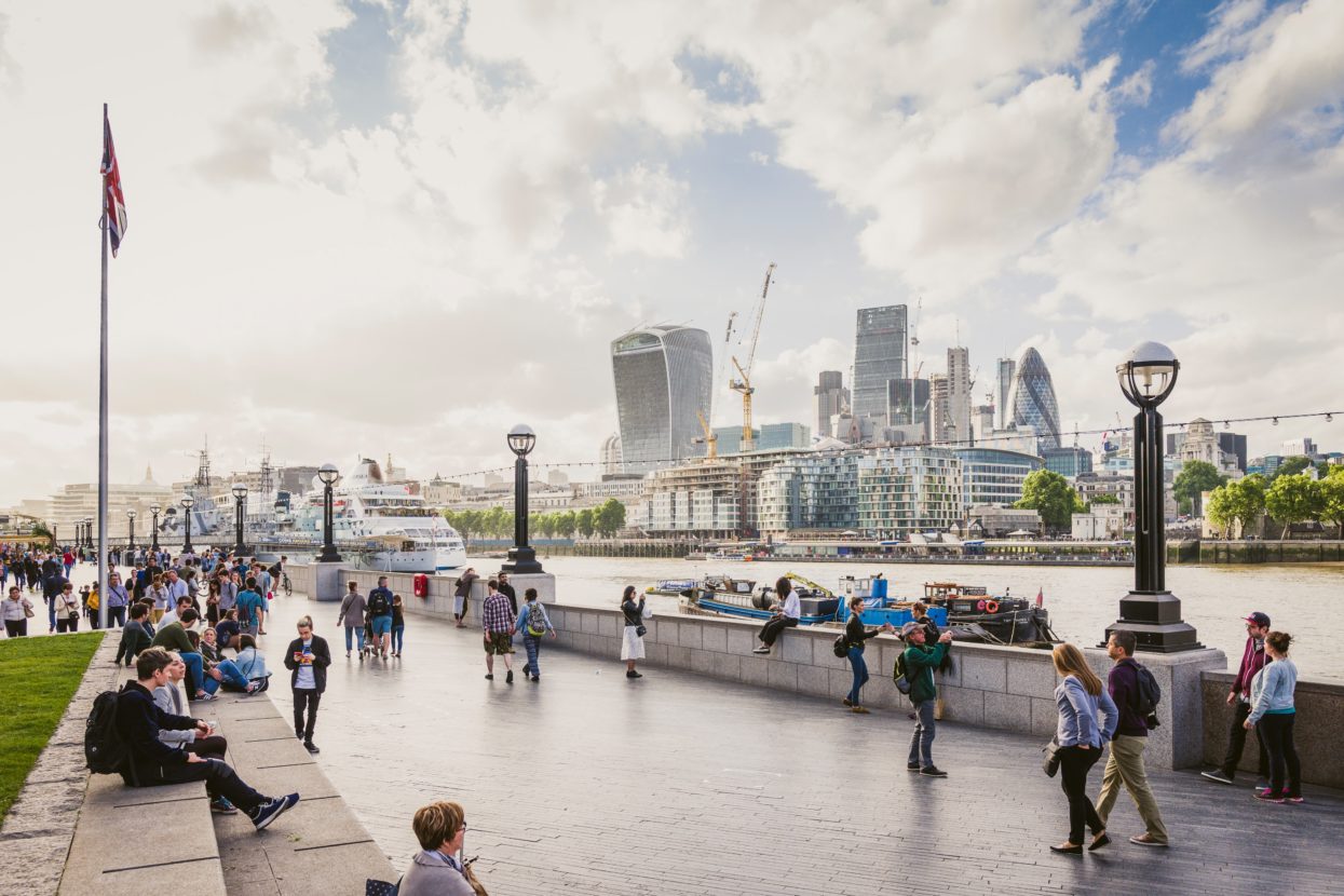 people socialising and walking along the river Thames with a view of the city across the river